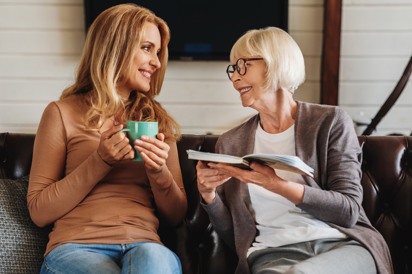 Mature women reading book with her daughter drinking coffee at home