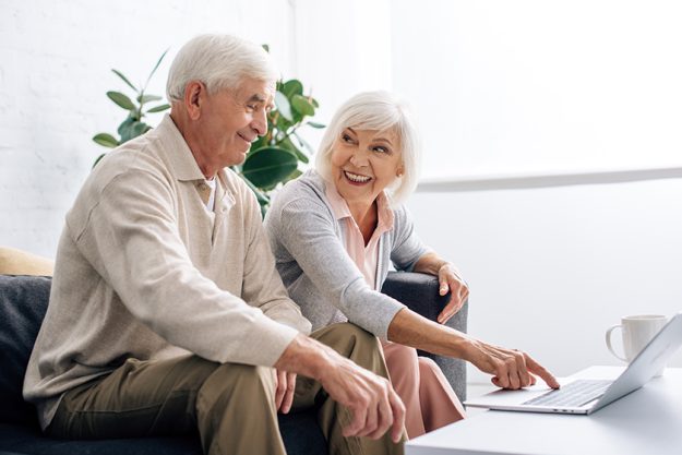 husband and smiling wife using laptop and sitting on sofa in apartment husband and smiling wife using laptop and sitting on sofa in apartment