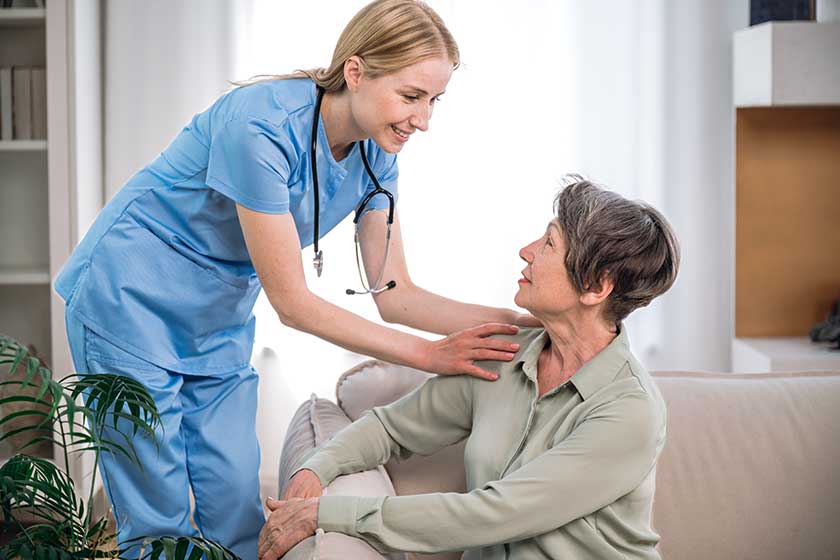Support and medical care at home. Smiling professional physician or nurse touching shoulders of senior female at appointment. Doctor visiting and consulting patient Support and medical care at home. Smiling professional physician or nurse touching shoulders of senior female at appointment. Doctor visiting and consulting patient