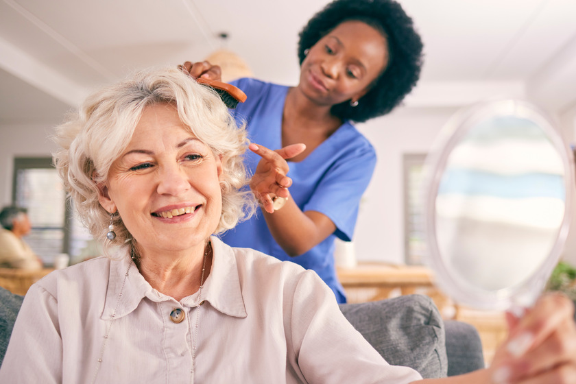 Caregiver brush hair of happy senior woman in the living room of the modern retirement home for self care. Mirror, routine and African female nurse doing a hairstyle for an elderly patient in lounge. 8 Reasons Why Reassurance Matters In Assisted Living Homes In Madisonville, LA