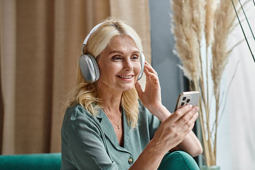 Cheerful middle aged woman in wireless headphones listening music Cheerful middle aged woman in wireless headphones listening music