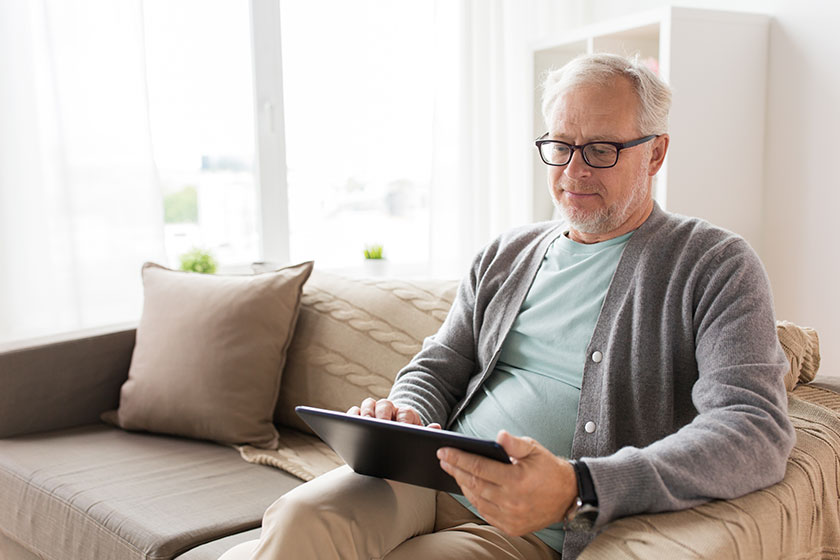 Senior man with tablet pc sitting on sofa at home