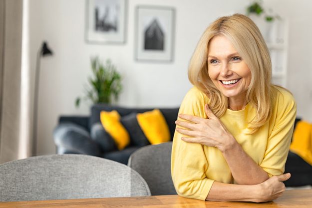 Close-up portrait on blonde-haired woman in home interior. Charming mature caucasian lady looking away and smiles, resting Close-up portrait on blonde-haired woman in home interior. Charming mature caucasian lady looking away and smiles, resting