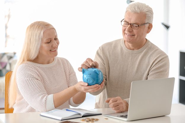 Mature-couple-putting-coin-into-piggy-bank-at-home. Mature-couple-putting-coin-into-piggy-bank-at-home.